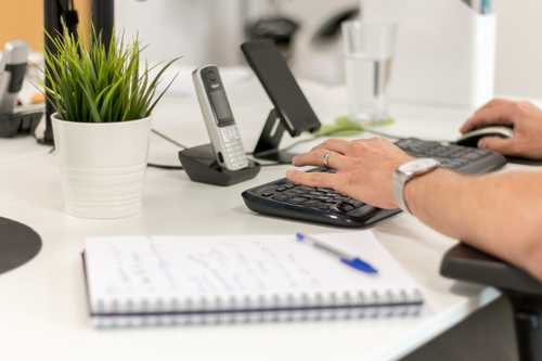 Photo of a digital agency white desk with notebook, keyboard, phone and plant
